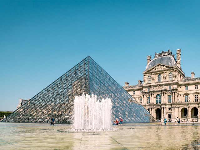 Fountain in front of glass pyramid and exterior of Louvre Museum in Paris, France