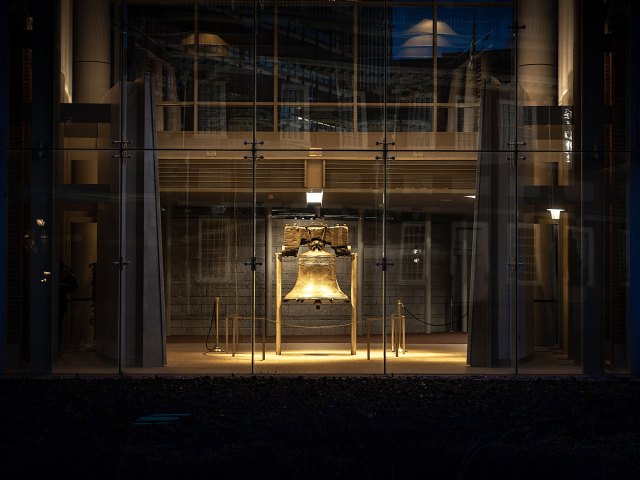 A picture of the Liberty Bell illuminated by light through a glass door at night