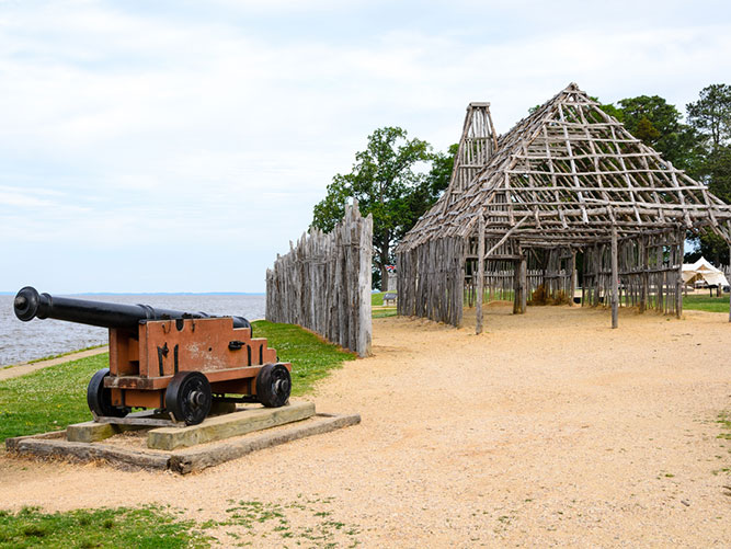 A thatched wooden house with a cannon outside