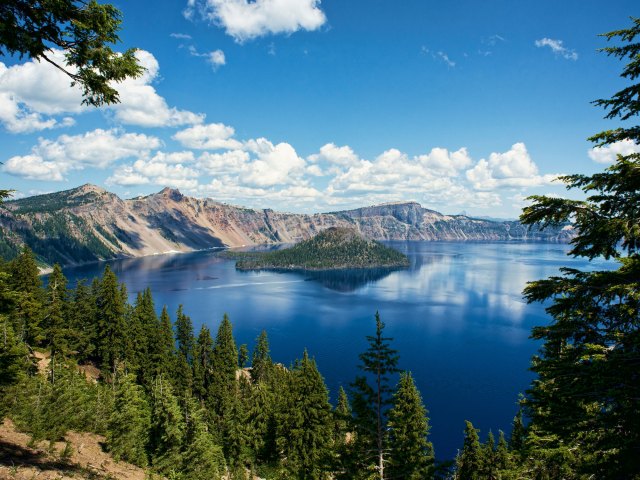 A picture of Crater Lake on a sunny day surrounded by pine trees