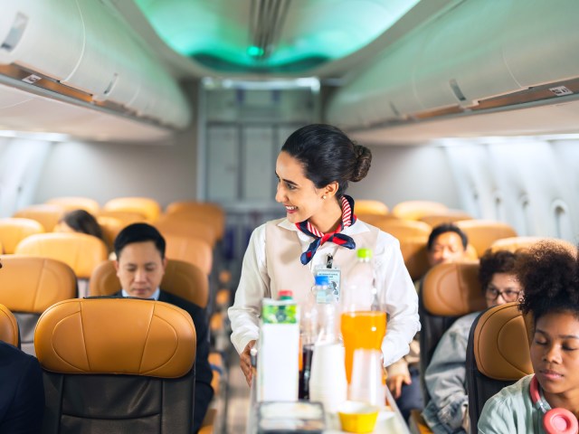 Flight attendant in airplane aisle serving passengers from beverage cart