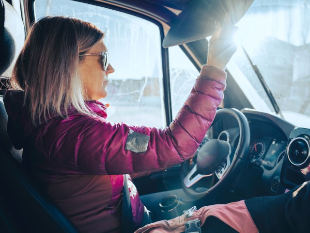 Driver wearing sunglasses and using window shade against sun