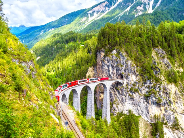 Bernina Express train on bridge leading to mountain tunnel in Switzerland